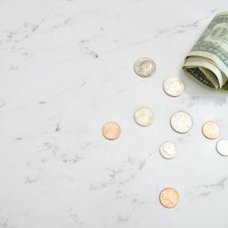 Rolled-up dollar bill and several coins on a marble counter