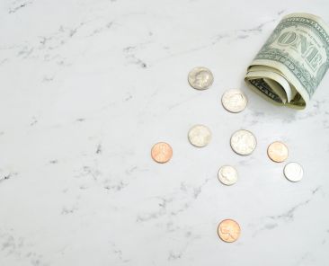 Rolled-up dollar bill and several coins on a marble counter