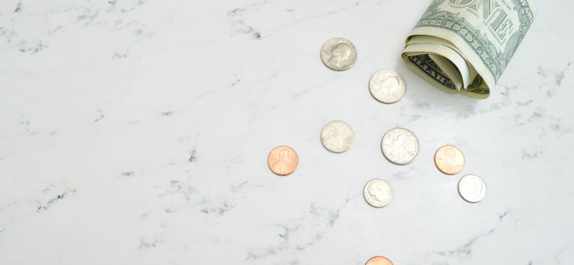 Rolled-up dollar bill and several coins on a marble counter