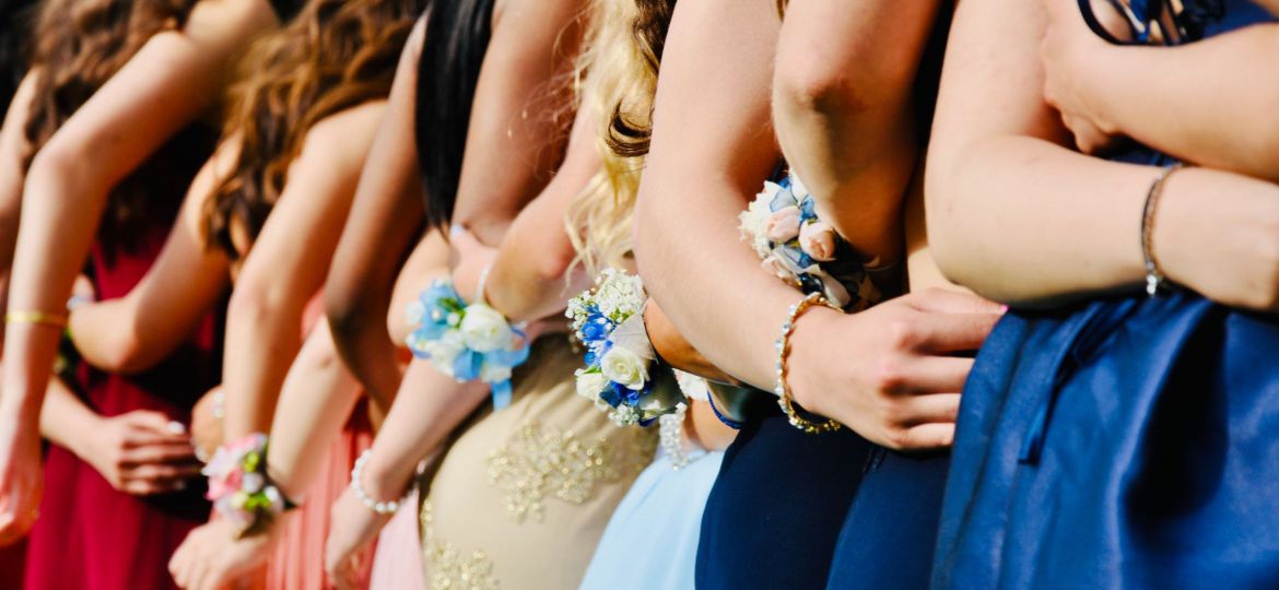 The photo depicts a group of girls posing for a photo in prom dresses.