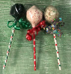 Three of Marsha's Specialty Desserts Cake Pops, each of which are presented with festive holiday-printed sticks and ribbons.