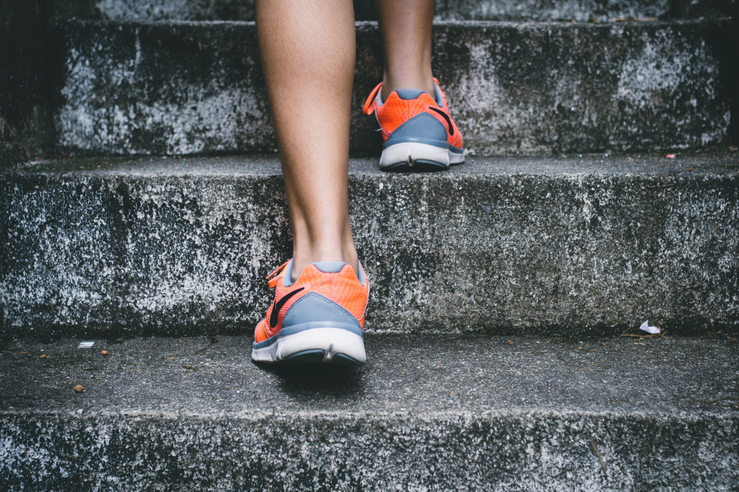 Woman's feet wearing orange and gray running shoes, running up concrete steps