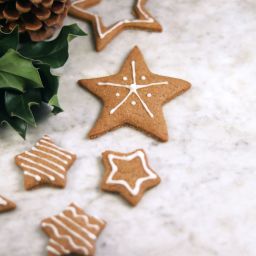 Gingerbread star shaped cookies next to pine cones and holly leaves