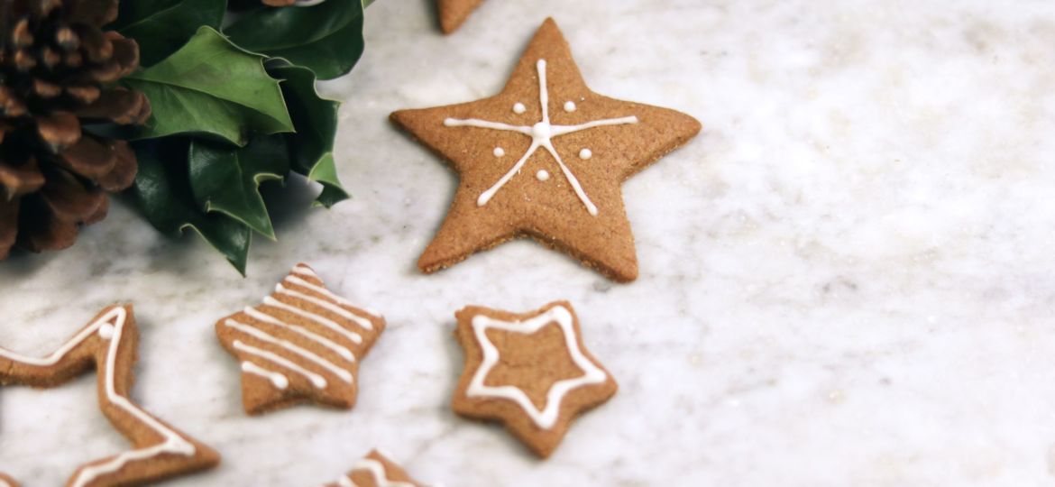 Gingerbread star shaped cookies next to pine cones and holly leaves