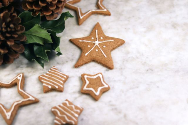Gingerbread star shaped cookies next to pine cones and holly leaves