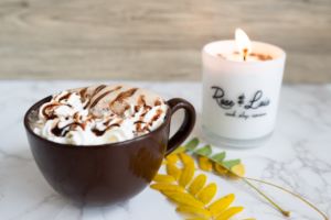 A mug of hot chocolate from Rose & Lois next to a candle