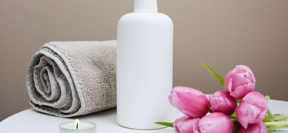 Image of rolled up towel, lotion, pink flowers and a lit tea light candle