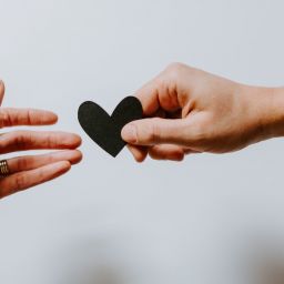 One hand handing a black heart to another hand