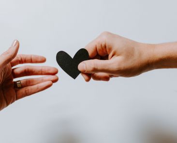 One hand handing a black heart to another hand