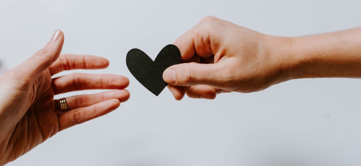 One hand handing a black heart to another hand
