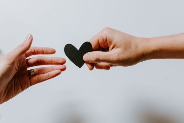 One hand handing a black heart to another hand