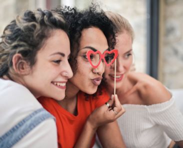 A photo of three women smiling with heart-shaped glasses for Galentine's Day