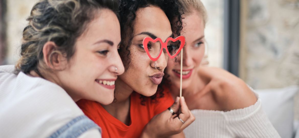 A photo of three women smiling with heart-shaped glasses for Galentine's Day