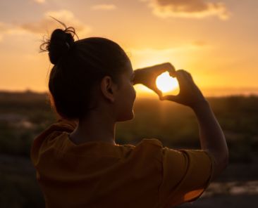 A photo of a woman holding a heart against the sun