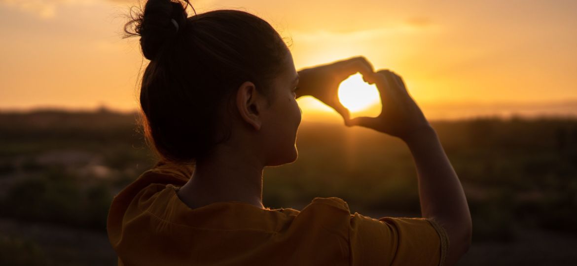 A photo of a woman holding a heart against the sun