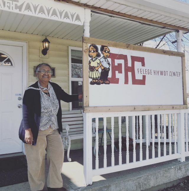 A photo of a woman standing next to a sign that reads FHC