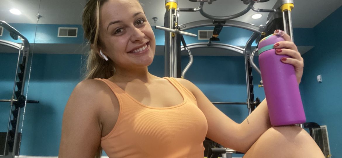 A photo of a girl in workout clothes holding a water bottle and smiling