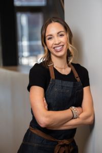 A photo of a woman (Kelsey Murphy) in an apron leaning on a wall