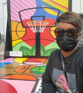 A photo of Shaunte next to a large mural of a basketball hoop