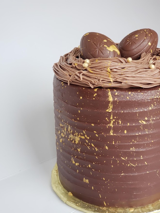 A photo of a chocolate cake with two cadberry eggs on top and gold decoration