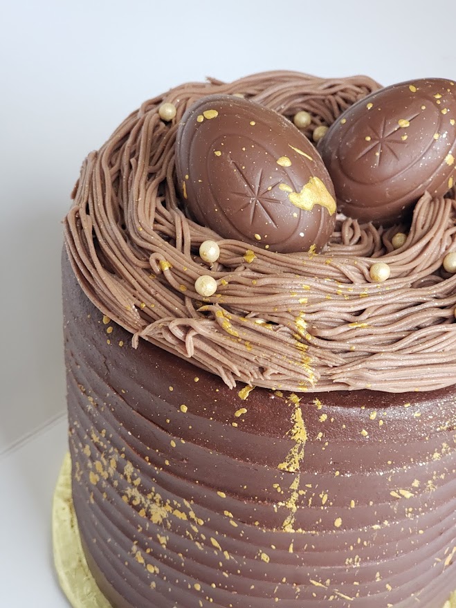 A different angle of the photo of a chocolate cake with two cadberry eggs on top and gold decoration