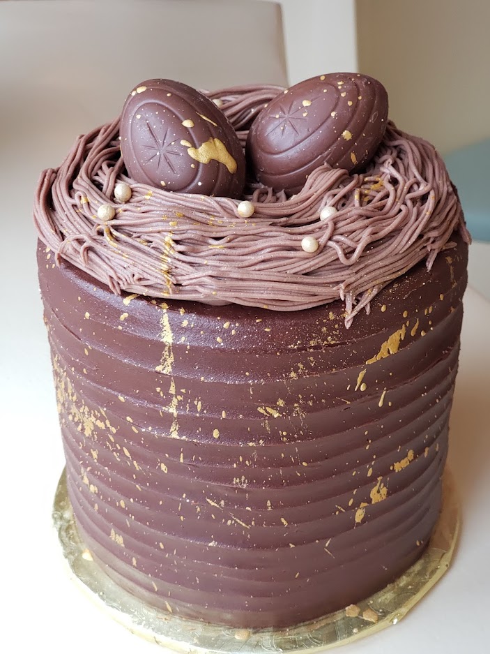A different angle of the photo of a chocolate cake with two cadberry eggs on top and gold decoration