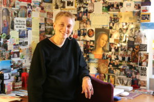 A photo of a woman sitting at a desk with many pictures on the walls behind her
