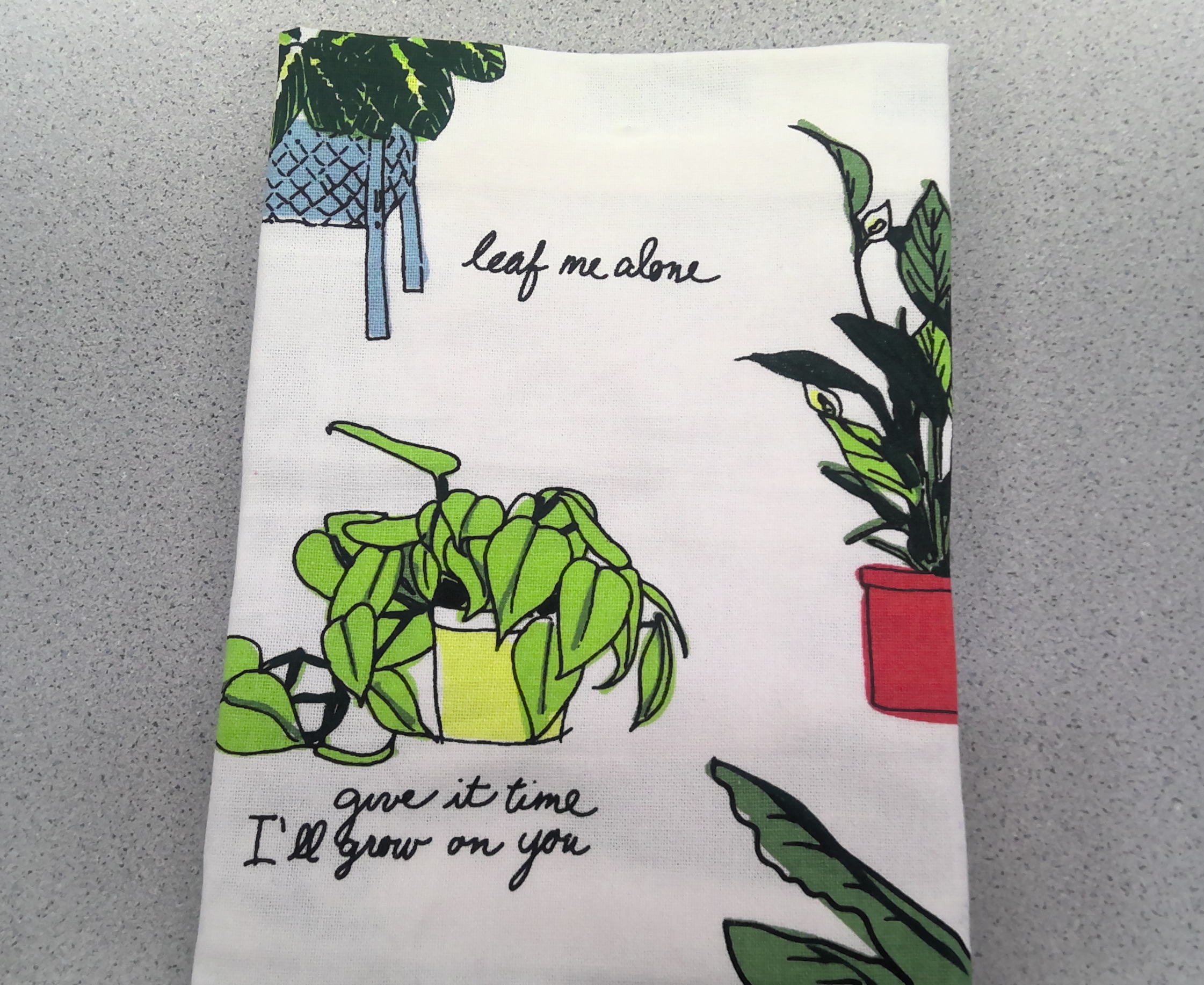 A photo of a tea towel that says "leaf me alone" and "give it time, I'll grow on you"