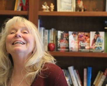 A photo of a woman smiling with a bookshelf behind her