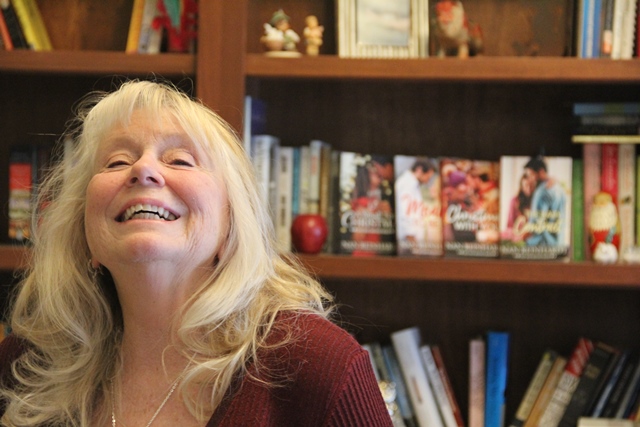 A photo of a woman smiling with a bookshelf behind her