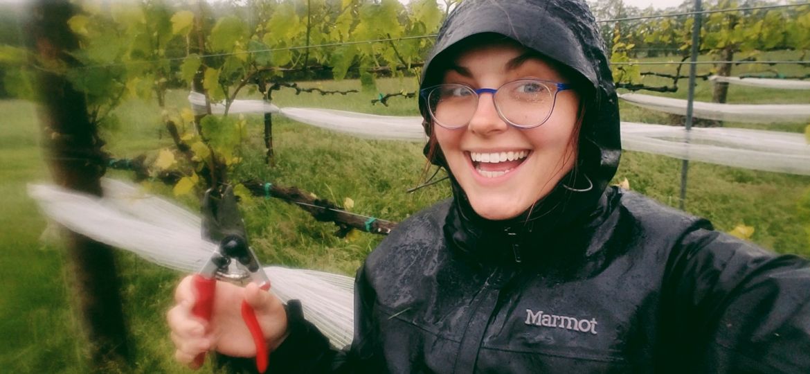 A photo of a woman from Oliver Winery in a rain coat smiling with clippers