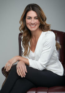 A photo of Lauren Schregardus in a white business casual shirt sitting with her hands crossed