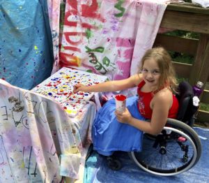 Riley little girl in wheelchair smiling and painting on a tapestry