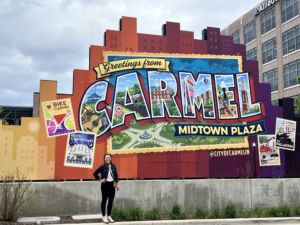 a woman standing in front of a colorful sign that says carmel