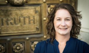 woman with short brown curly hair wearing navy blue collared shirt smiles with teeth