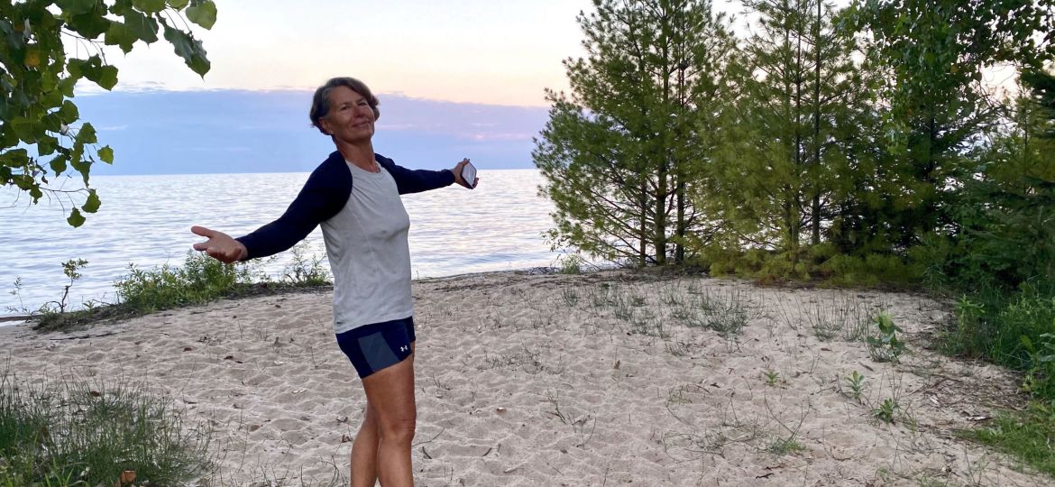 A photo of a woman with her arms out by a lake