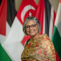 older woman with gray hair smiling in front of foreign flags
