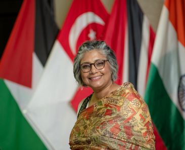 older woman with gray hair smiling in front of foreign flags