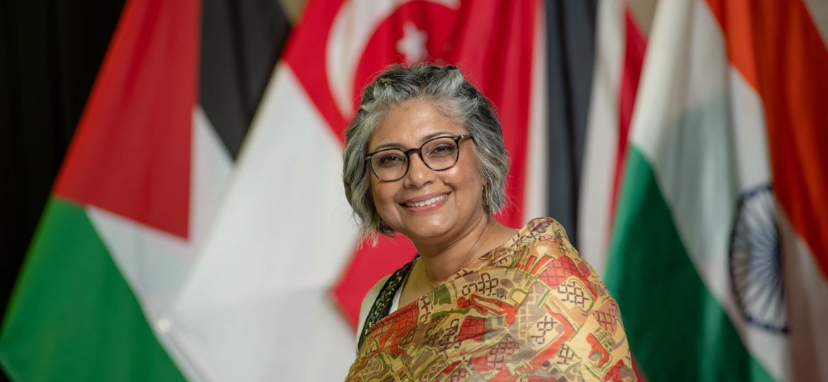 older woman with gray hair smiling in front of foreign flags