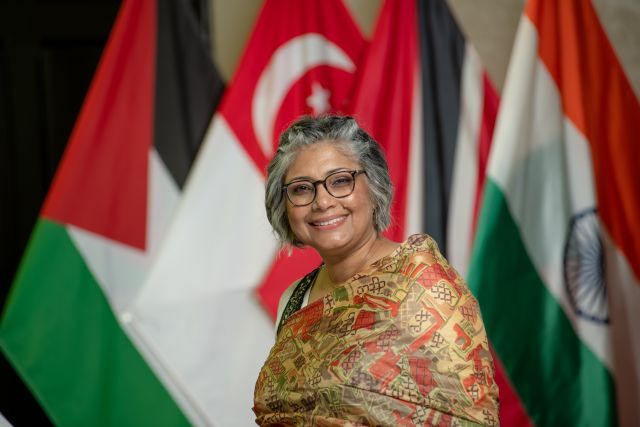 older woman with gray hair smiling in front of foreign flags