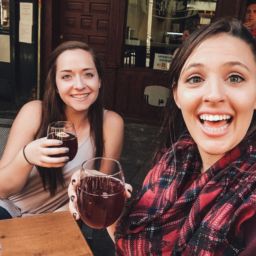 two women holding glasses of red wine smiling sitting at a table
