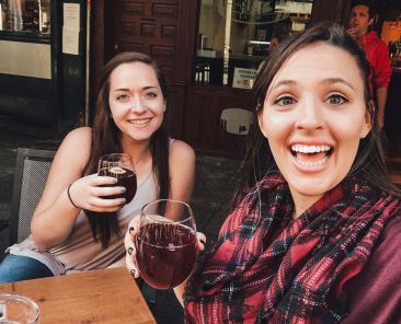 two women holding glasses of red wine smiling sitting at a table