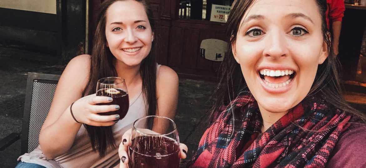 two women holding glasses of red wine smiling sitting at a table