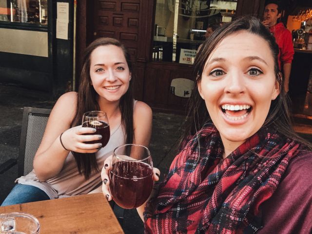 two women holding glasses of red wine smiling sitting at a table