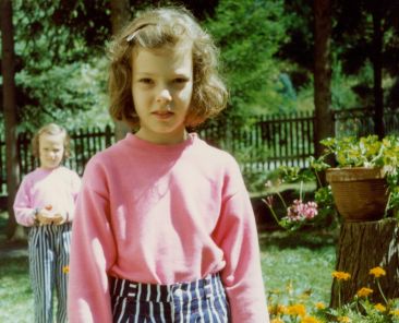 little girl wearing pink swear and blue and white striped pants with curly brown hair