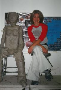 woman with short hair smiling next to clay sculpture replica of her