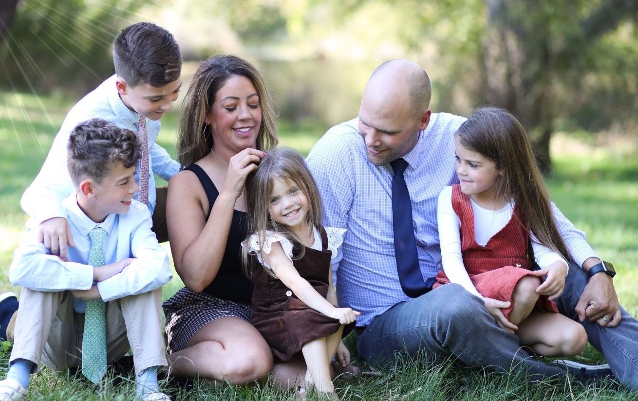 family of six sit on grass and smile and pose for family photos