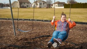 a young woman with a disability smiles as she swings on the park swing