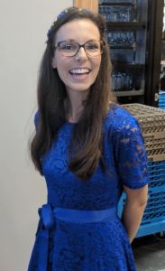 woman wearing blue lacy dress with glasses and brown hair smiles widely