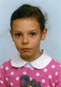 little girl with a straight face wearing a pink polka dot shirt with a white collar